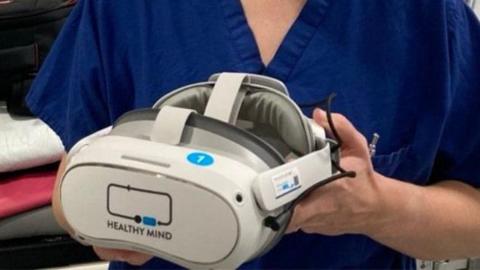A woman in nursing scrubs holding a virtual reality headset