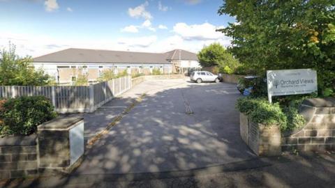 A car park entrance alongside a sign saying 'Welcome to Orchards View Residential Care Home'.