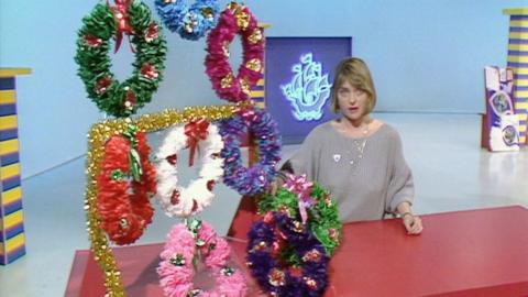 Janet Ellis stands beside nine different coloured Christmas garlands