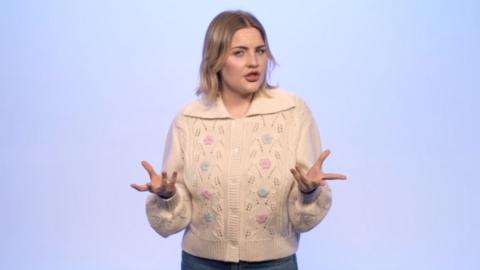 Mared Parry who has blonde hair and a nose ring in a white cardigan in front of a pale blue background
