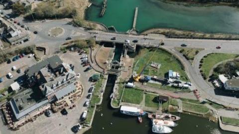 In the middle of the picture is a river that runs in the middle of land. A road goes across the river, and on either side are buildings. 