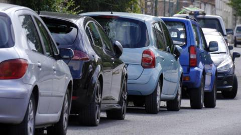 A line of cars parallel parked on the edge of a street.