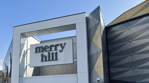 The modern frontage of a shopping centre, with the words Merry Hill set in a large suspended sign