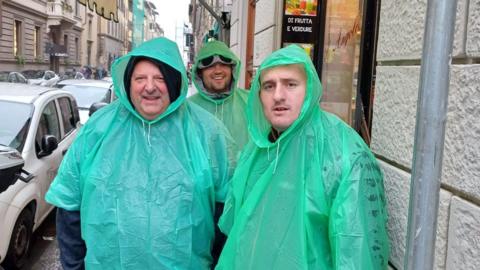 John Lumley and two other men standing in an Italian street in the rain, wearing green ponchos