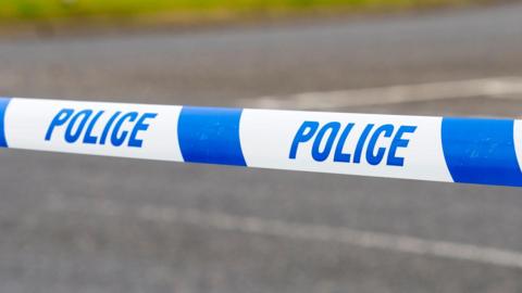 A generic close up picture of a blue and white plastic police tape pulled across a road. 
