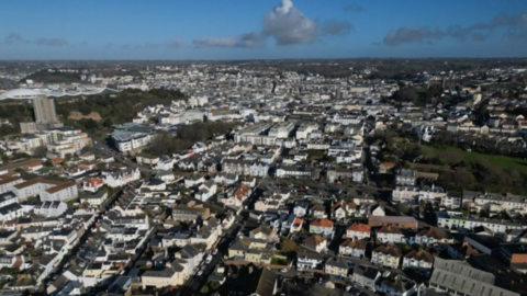 Ariel shot of South St Helier, Jersey. There are rows of houses and buildings below. The photo was taken on a cloudy day.
