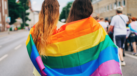 Two people with Pride flag wrapped round their shoulders