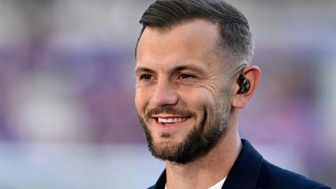 Jack Wilshere is shown smiling, with an earpiece in his left ear