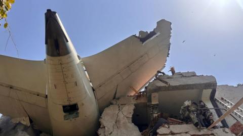 Part of the wreckage of the plane sits on top of a partially destroyed building