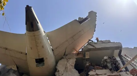 Part of the wreckage of the plane sits on top of a partially destroyed building
