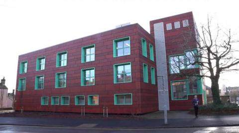 Voreda House office block in Penrith. The three-storey red building has green windows and is made up of a main block, with a tower next to it, in the same style and colours.
