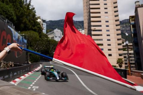 A marshal waves a red flag at the Monaco Grand Prix, in front of Lewis Hamilton driving his Mercedes W15 car.