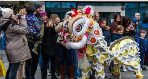 A multi-colured chinese dragong puppet is in front of a group of people of mixed ages standing next to eachother and smiling.