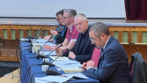 Two women and three men sitting at a table with microphones