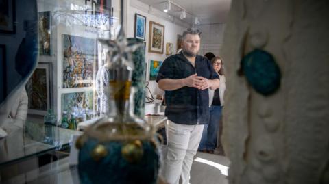 The artwork inspired by the seagrass and kelp projects on display in an exhibition space, with people milling around to look at the paintings, pottery and other work.