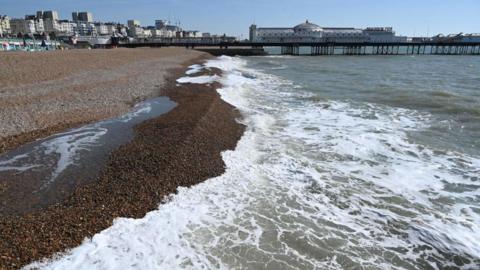 A pebbled-beach with sea foam washing up the shore.