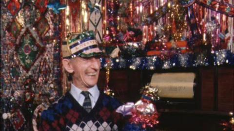 'Tinsel Man' Fred English smiling in his tinsel-covered living room, wearing a hat with tinsel on it.