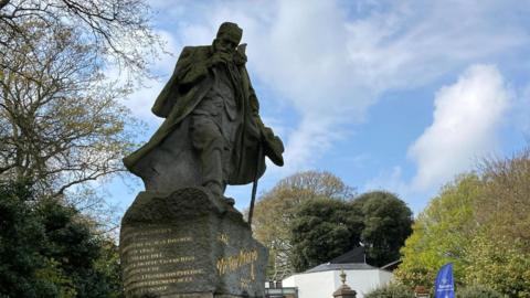 Victor Hugo statue in Candie Gardens, Guernsey, with buildings and trees in the background.