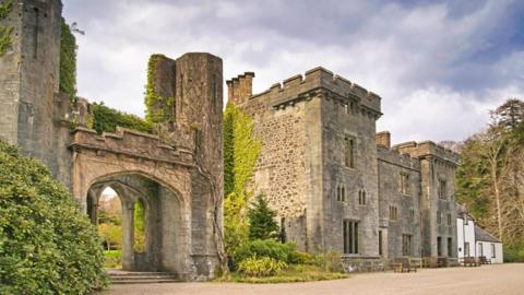 Skye's Armadale Castle is a ruin. There is an entrance with steps and a stone arch and large turreted property with narrow windows.