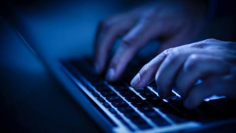 A pair of hands typing on a laptop keyboard in a dark room.