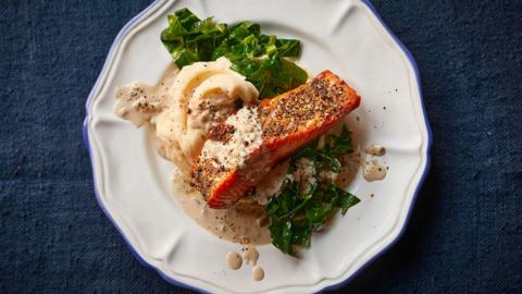 Image of Salmon au poivre, recipe from BBC Food. Salmon placed on top of mashed potato and steamed greens, served on a white plate.