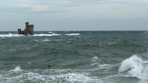 Choppy seas around the Tower of Refuge in Douglas Bay. The sea is dark and the sky is cloudy with a hint of blue.
