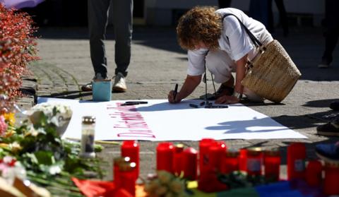 A woman writes on a placard near tributes placed on the ground following an incident in which several individuals were killed after a man randomly stabbed passers-by with a knife at a city festival, in Solingen, Germany, August 24, 2024. REUTERS/Thilo Schmuelgen