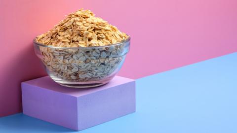 A bowl of rolled oats on a purple block with a pink and blue background