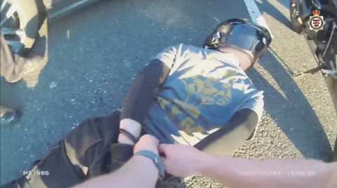 A man wearing black clothing and a black helmet lies on the ground with his hands behind his back as police arrest him