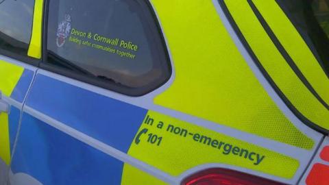 A Devon and Cornwall Police vehicle showing the side of the car and branding on the side. It is blue and yellow.