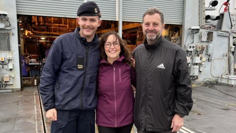 A son, his mother and father with arms around the shoulders smiling whilst standing onboard the HMS Richmond.