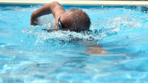 A man with goggles on doing freestyle in a pool.