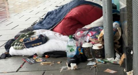 A sleeping bag surrounded by food cartons by a shop front on a wet street. 