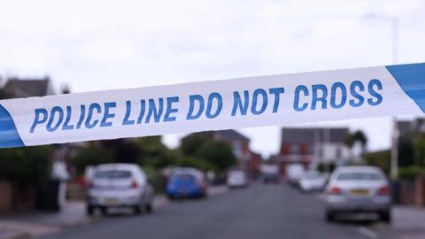 A stock image of police tape cordoning off a residential street.