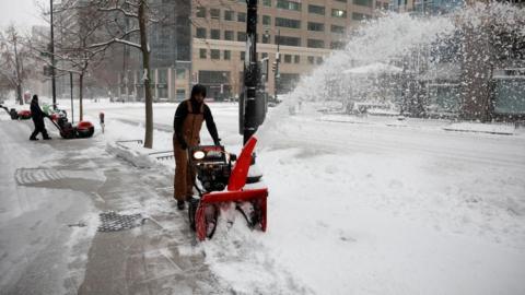 A man with a large red machine taking snow off the pavement