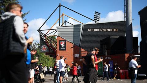 The outside of the AFC Bournemouth stadium. It is a red brick building with black cladding that reads 'AFC Bournemouth' and has a red and black Bournemouth logo on.