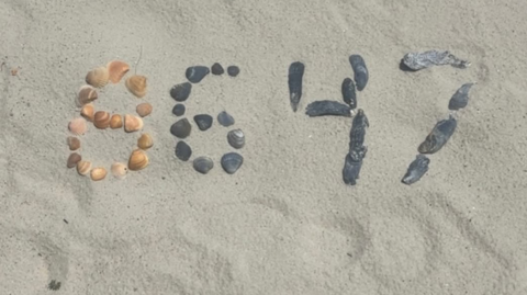 A group of stones in some sand arranged to depict the numbers 8647