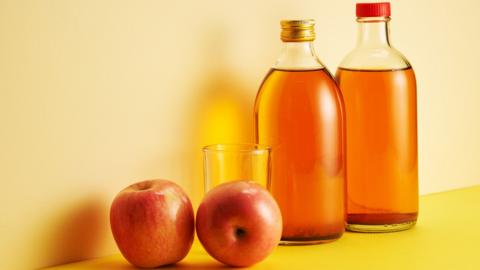 Bottle of apple cider vinegar and fresh apple against yellow background