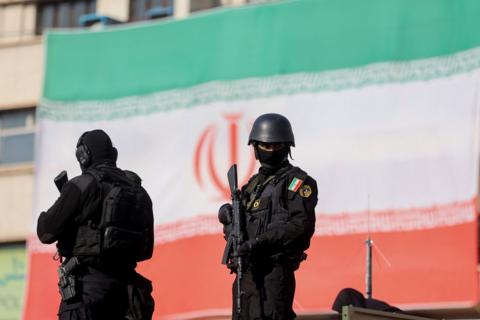Armed police in Tehran - two figures can be seen with a giant Iranian flag hanging behind them 