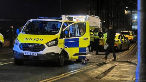 Police vans and a fire engine seen on a street by Chester station, with blue lights flashing and officers gathered on the road.