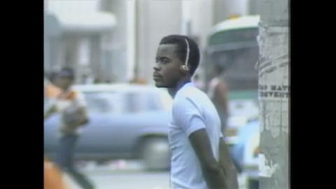 A man in a blue tshirt listens to music on his headphones, in the street.