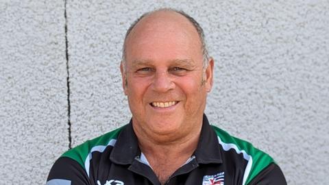 Headshot of Steve Worrall smiling, standing against a white outside wall, wearing a Chew Valley RFC top