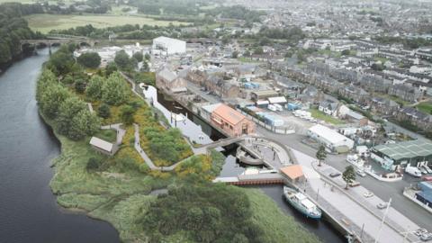 An aerial view of Annan harbour showing landscaped walkways bordering the river and separating waterways with a bridge and small dam, as well as a number of buildings