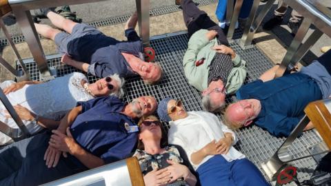 People laid on steel grid that was installed over the River Sheaf at Sheffield Station. They are laid so their heads almost meet in the middle.