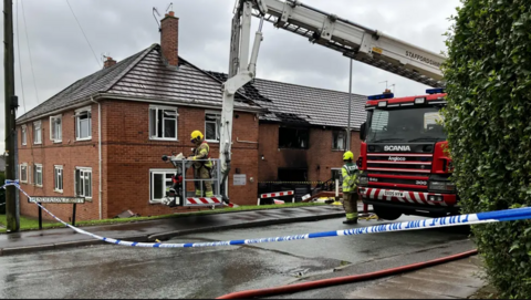 Firefighters at the scene of the fire by a fire engine and crane in Meir