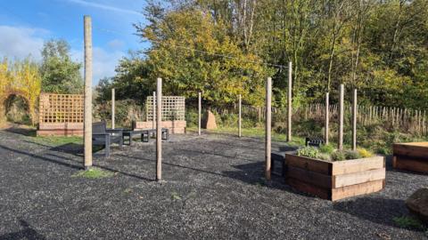 A planting area with wooden pots and benches surrounded by trees