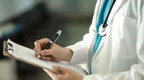 A doctor writing with a pen on a piece of paper on a clipboard 