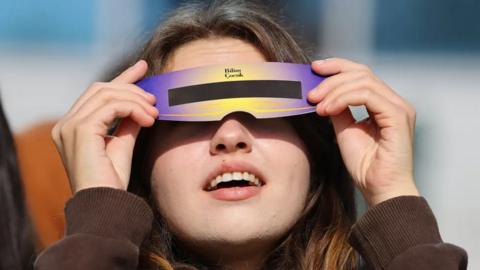 Close-up of a person holding up special glasses to view the solar eclipse.