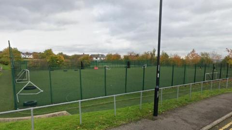 A black wire fence surrounds a number of artificial football pitches.