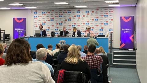 Scene at the stadium with the panel at the front, in front of a crowd of fans 